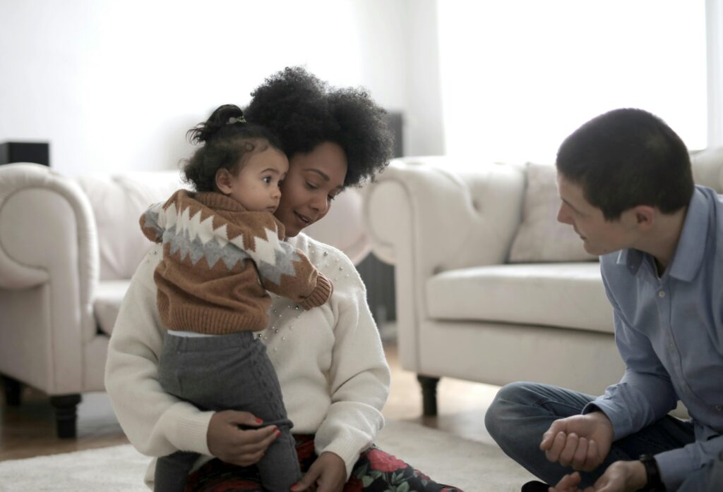 Man, woman, and small child interact in the bright living room on the floor.