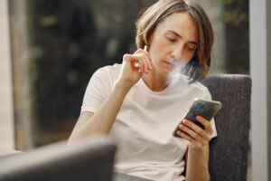 picture of a lady smoking a vape pen while looking at mobile device.